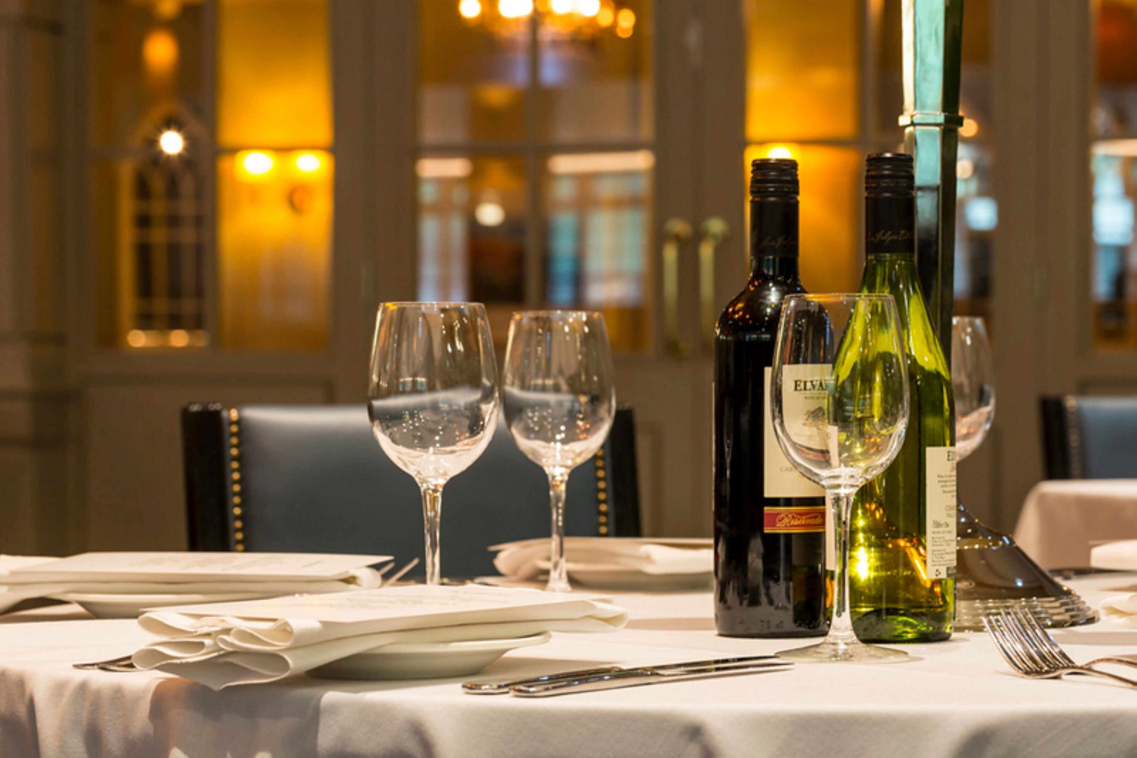 Una mesa de comedor dispuesta con copas de vino, botellas y cubiertos.