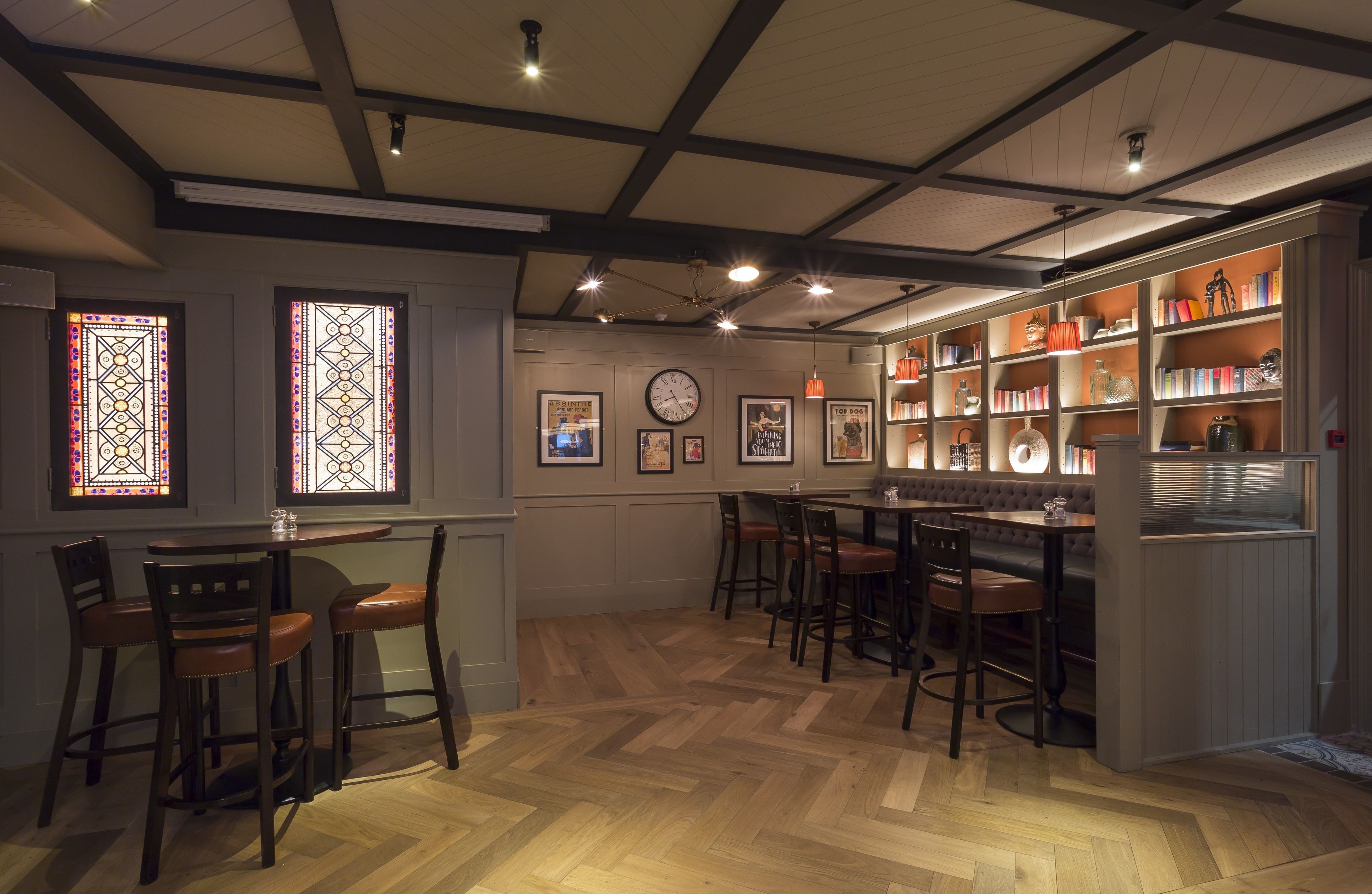 Un espace bar doté d’un plancher en bois, de tabourets de bar et d’une bibliothèque remplie de livres et d’objets décoratifs.