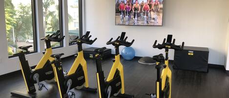 A gym with stationary bikes, a large TV screen, and exercise balls.