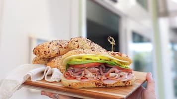 A sandwich on a wooden board held by a person, with a sign reading "New River Cafe & Bakery" in the background.