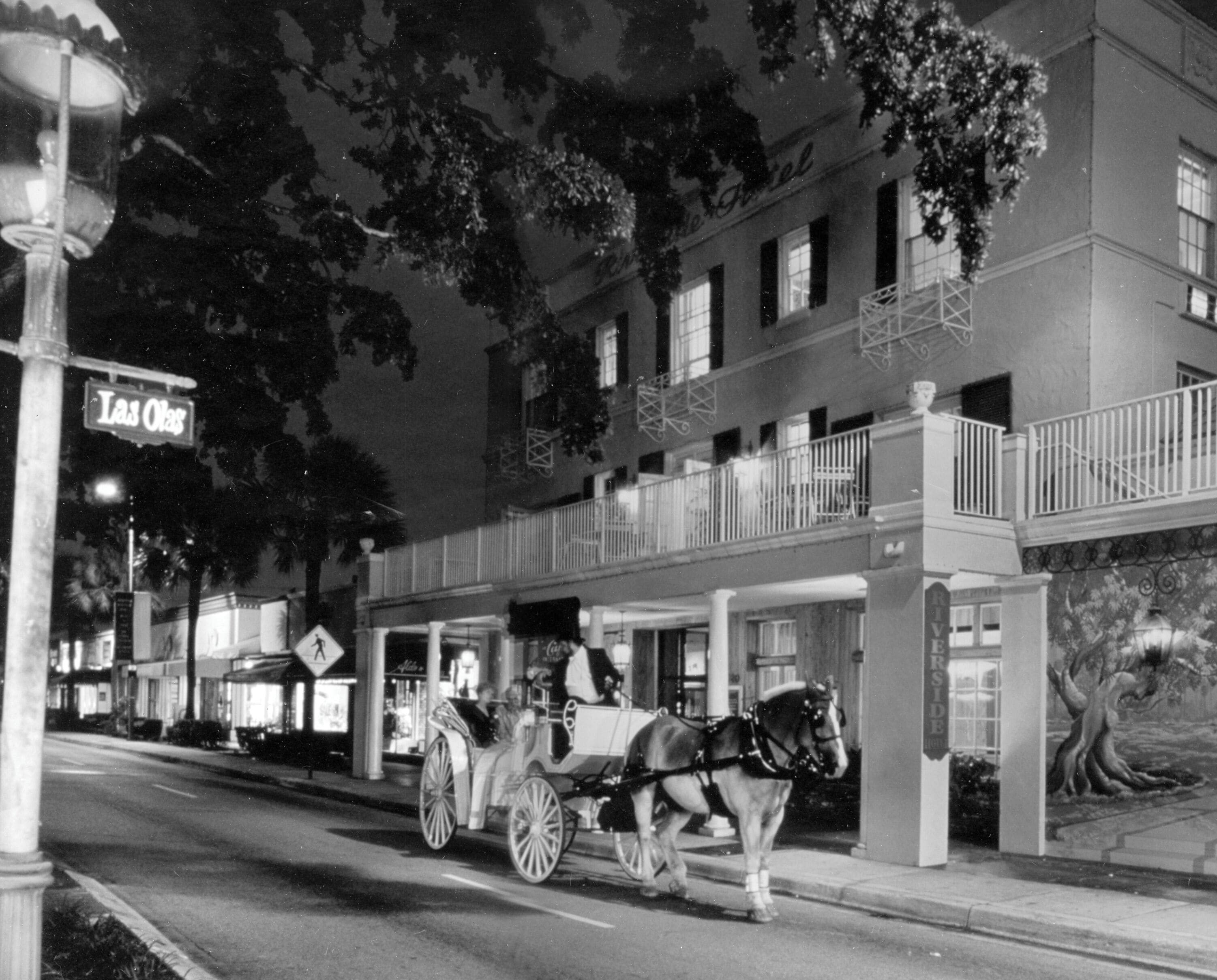 A horse-drawn carriage on a city street at night, with buildings and a sign that reads 'Las Olas.'