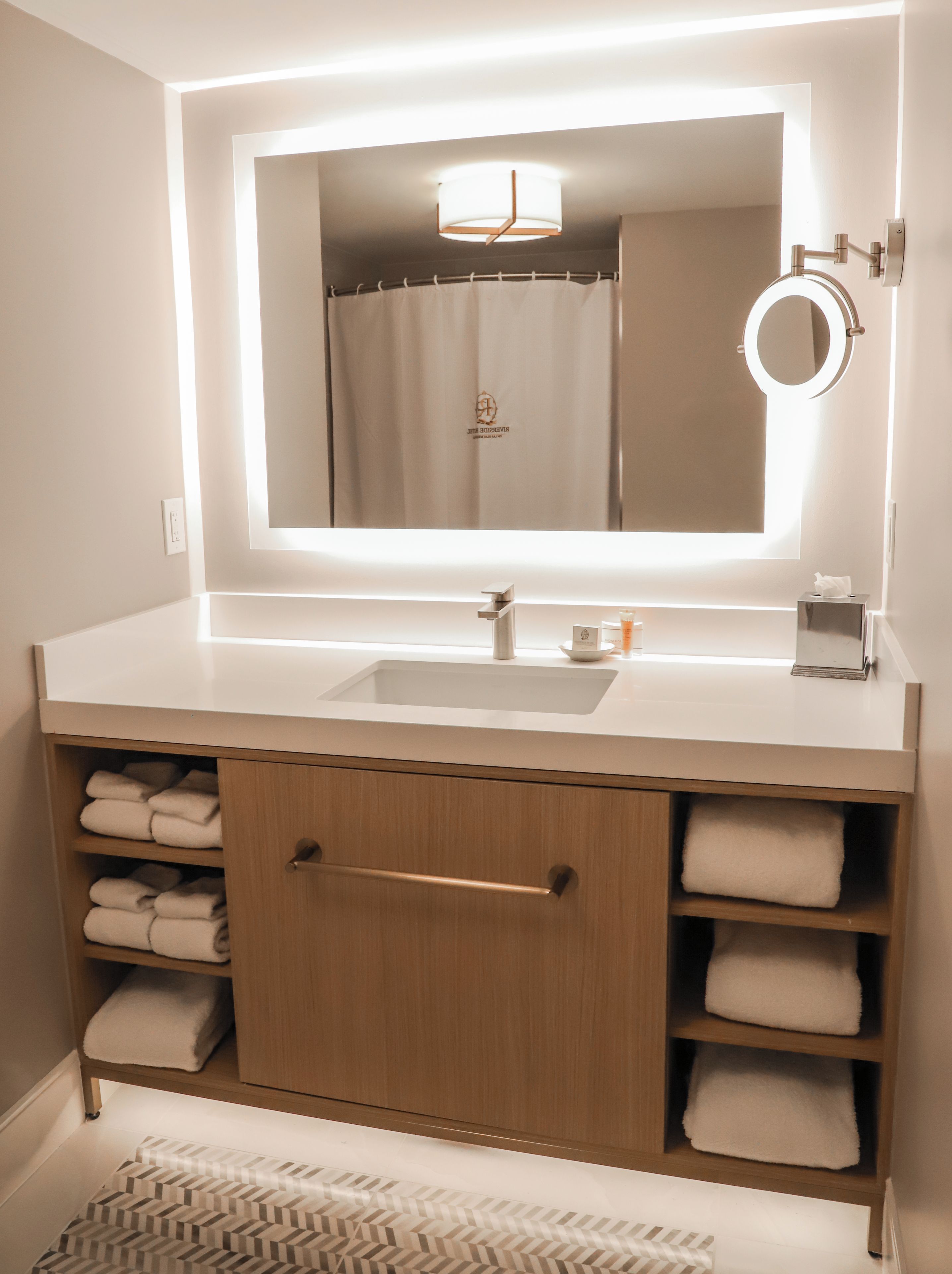 A bathroom with a large mirror, a sink, and a towel rack.