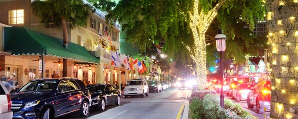 A street lined with buildings, some with flags, and cars parked along the road.