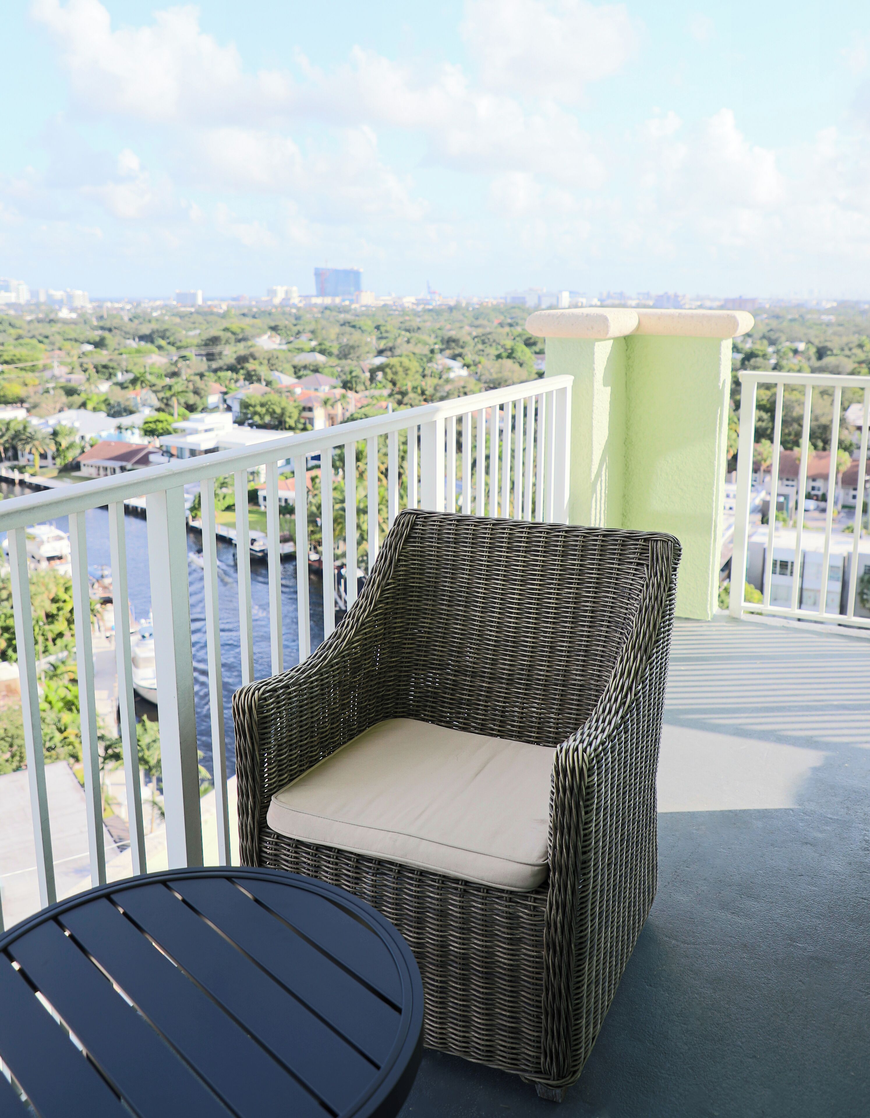 A wicker chair with a cushion on a balcony with a view of a cityscape and water.