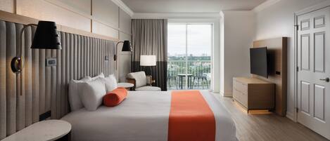 Une chambre d’hôtel moderne dotée d’un grand lit, de tables de chevet, d’une télévision et d’un balcon offrant une vue sur la ville.