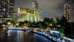 A waterfront hotel with a pool, palm trees, and high-rise buildings in the background.