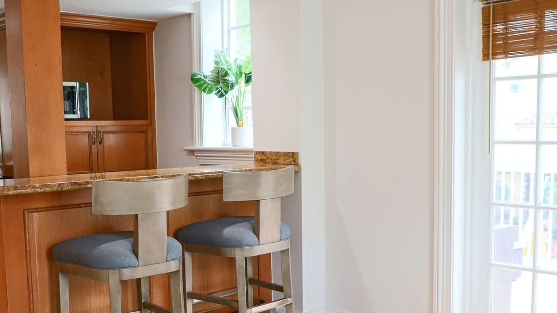 Una cocina con armarios de madera, un ventanal con una planta y dos taburetes de bar.