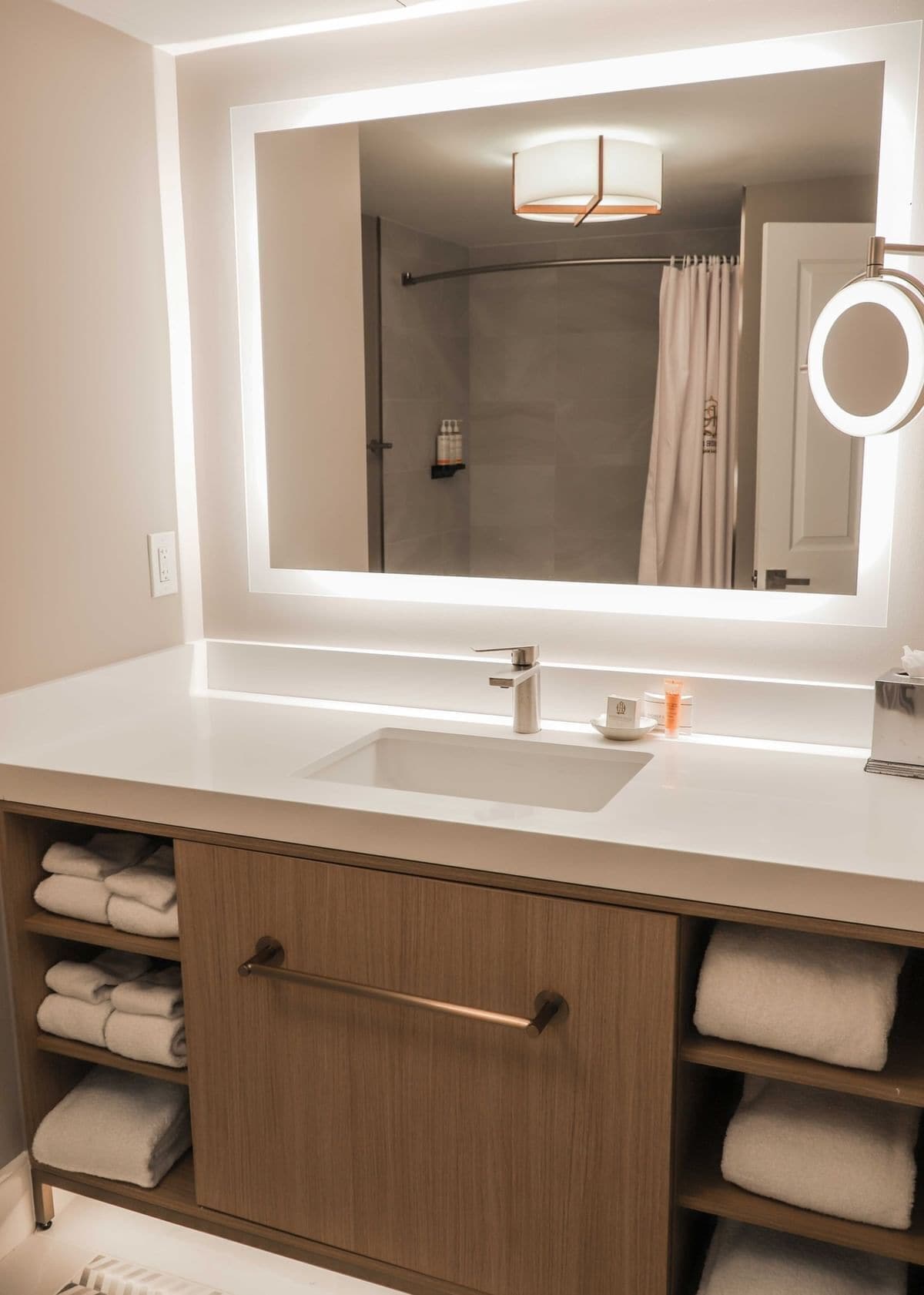 A bathroom with a large mirror, a sink, a towel rack, and a shower curtain.