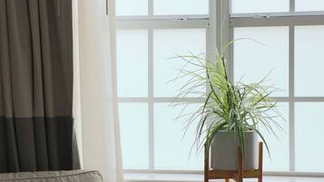 Una habitación con cama, una mesita con una planta en maceta y una ventana con cortinas.