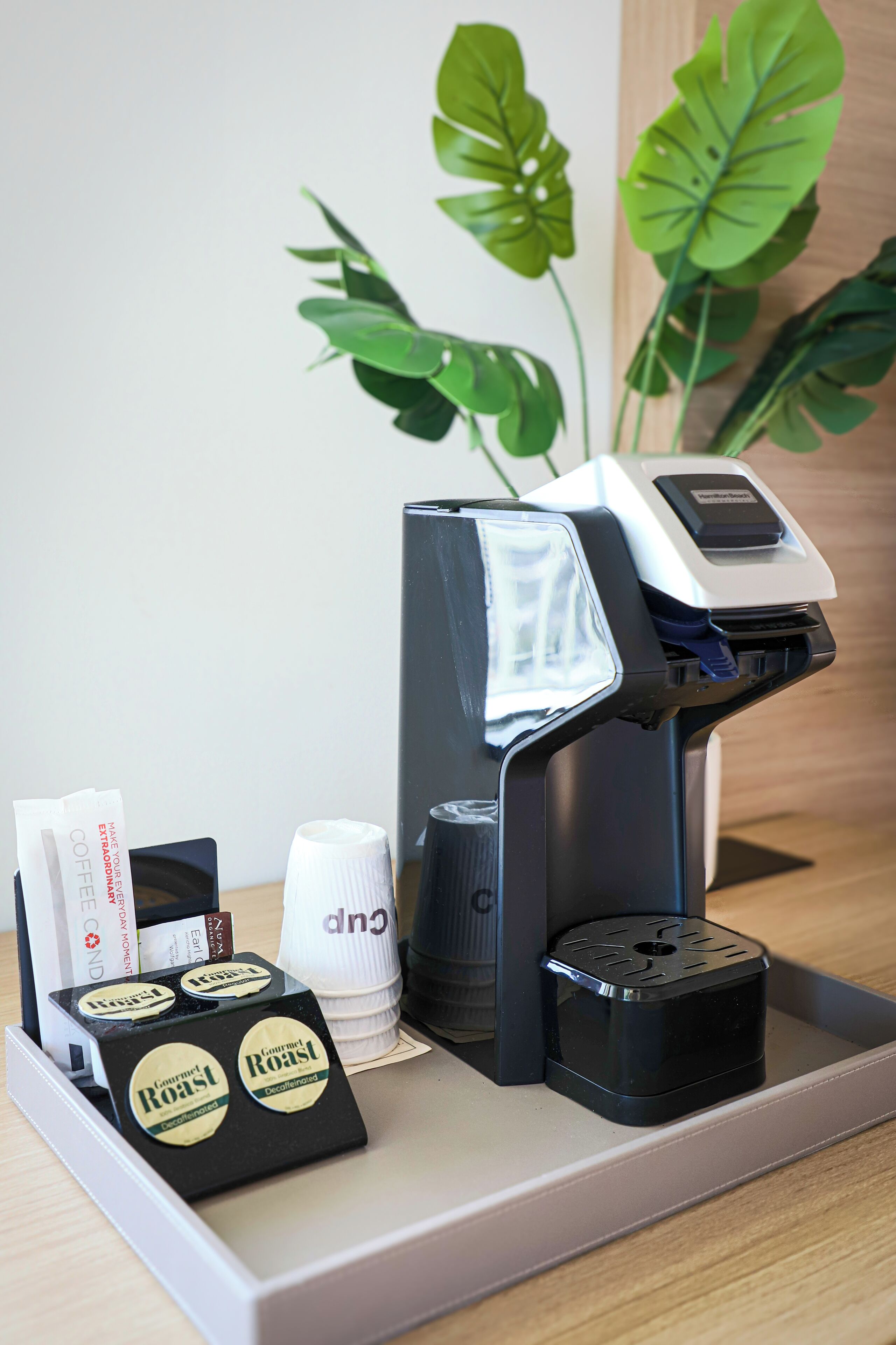 Une machine à café dotée d’un compartiment contenant des dosettes de café et des gobelets jetables.