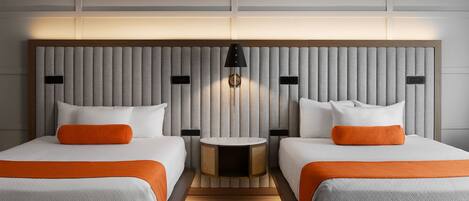 A hotel room with two beds, a round table, and a wall-mounted lamp.
