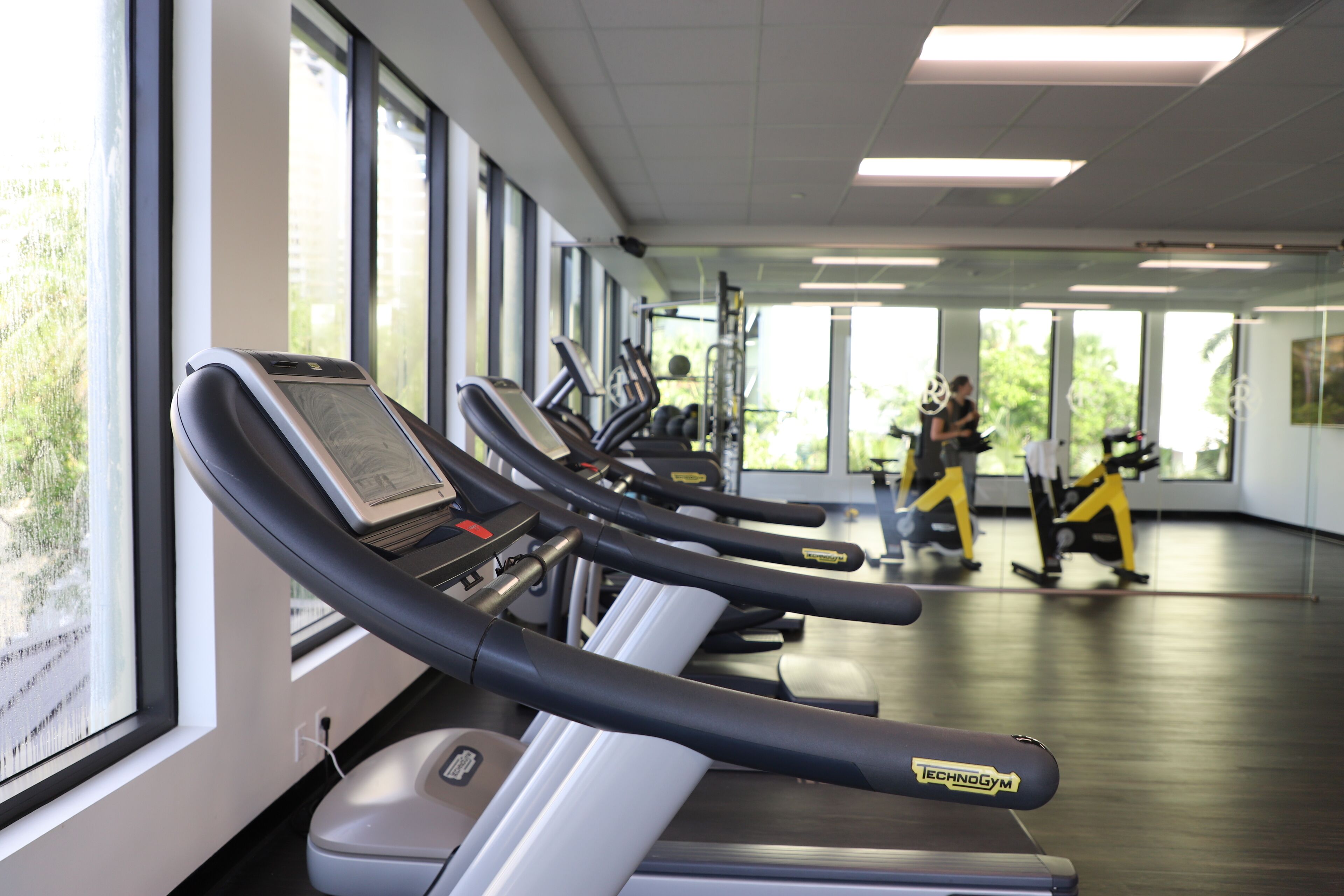 A gym with treadmills, exercise bikes, and a person walking in the background.