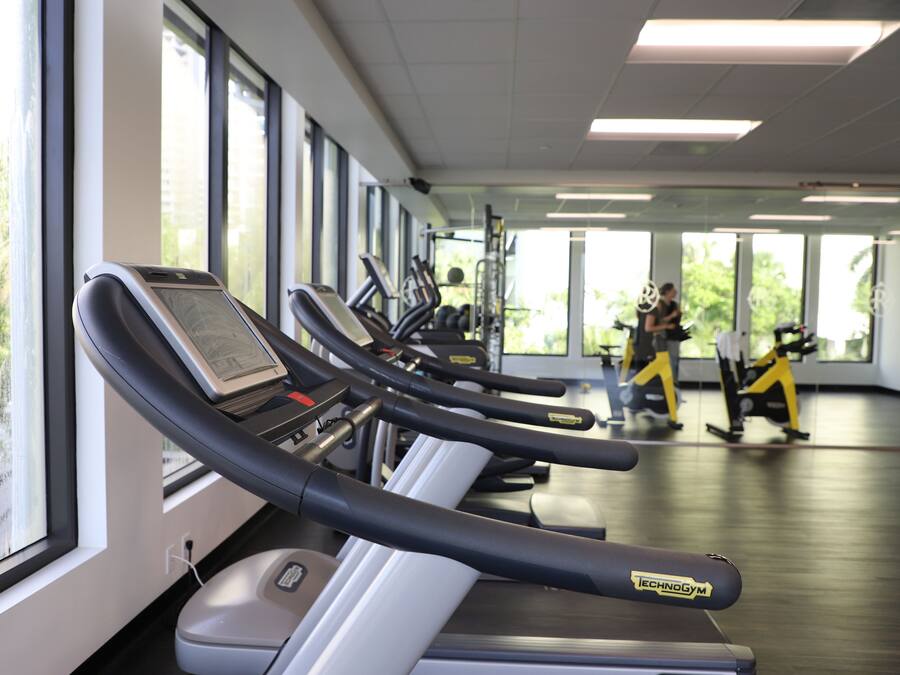 Un gimnasio con cintas de correr, bicicletas estáticas y una persona caminando al fondo.