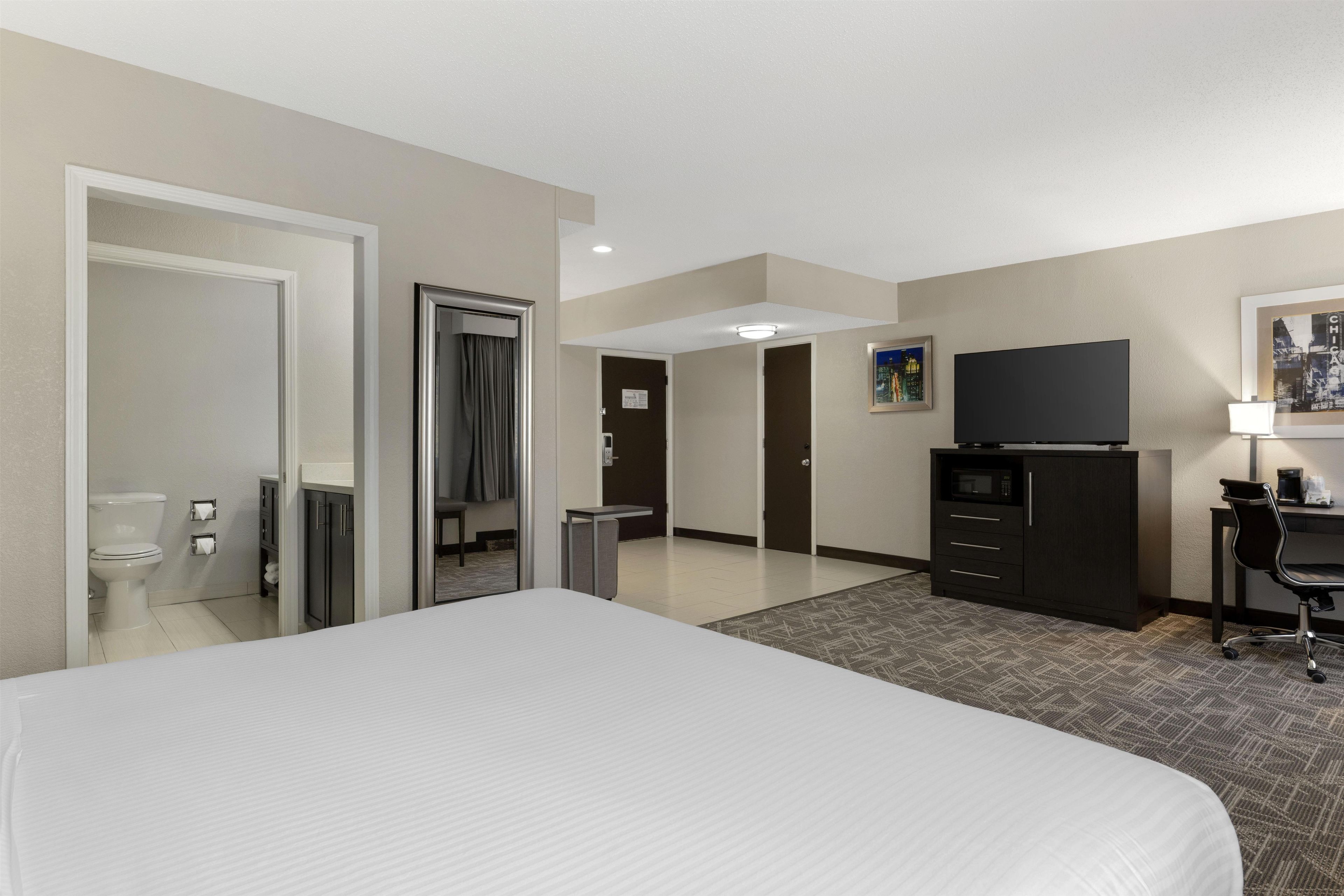 Une chambre d’hôtel avec un grand lit, une télévision, un bureau avec une chaise et un tableau au mur.