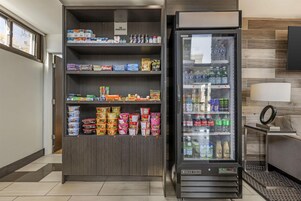 Máquina expendedora y vitrina refrigerada llenas de aperitivos y bebidas en un entorno comercial.