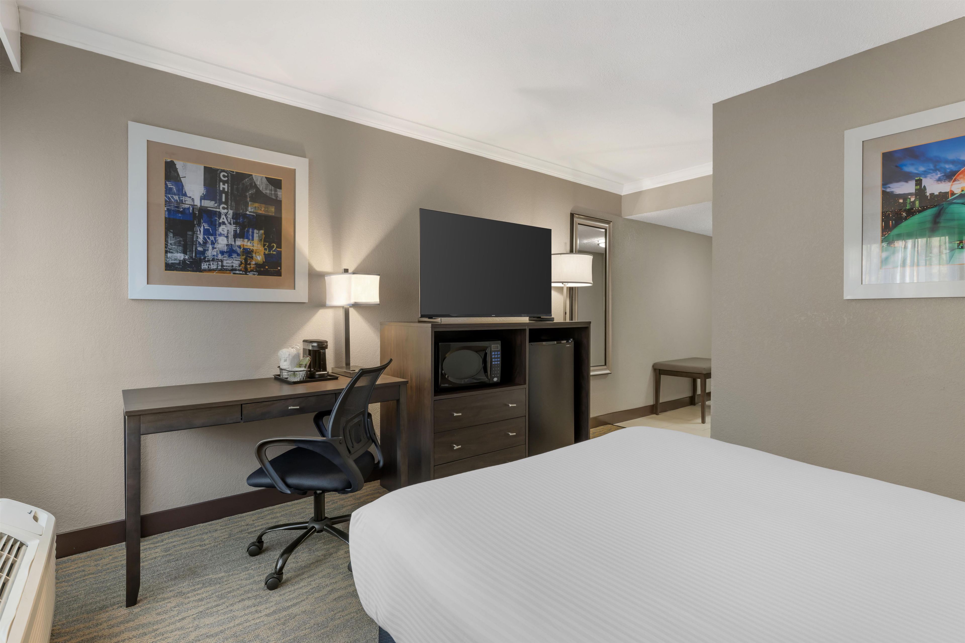 Une chambre d’hôtel comprenant un lit, un bureau avec une chaise, un téléviseur à écran plat, un four à micro-ondes, une machine à café et une petite table.