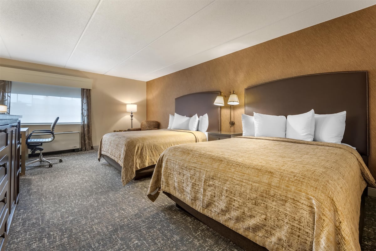 A hotel room with two beds, a desk, and a chair.