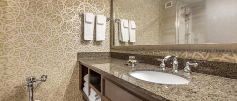 A bathroom with a patterned wall, a sink with a mirror, a toilet, and a shower.