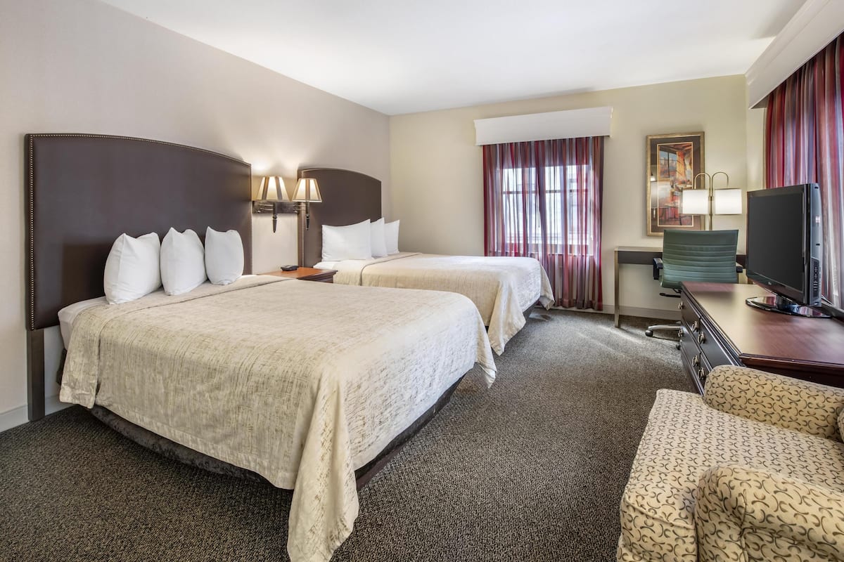 A hotel room with two beds, a desk with a television, a chair, and a painting on the wall.