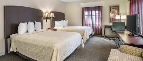 A hotel room with two beds, a desk with a television, a chair, and a painting on the wall.