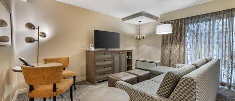 Habitación de hotel con sofá, dos sillones, una mesita redonda, televisor, armario y ventana con cortinas.