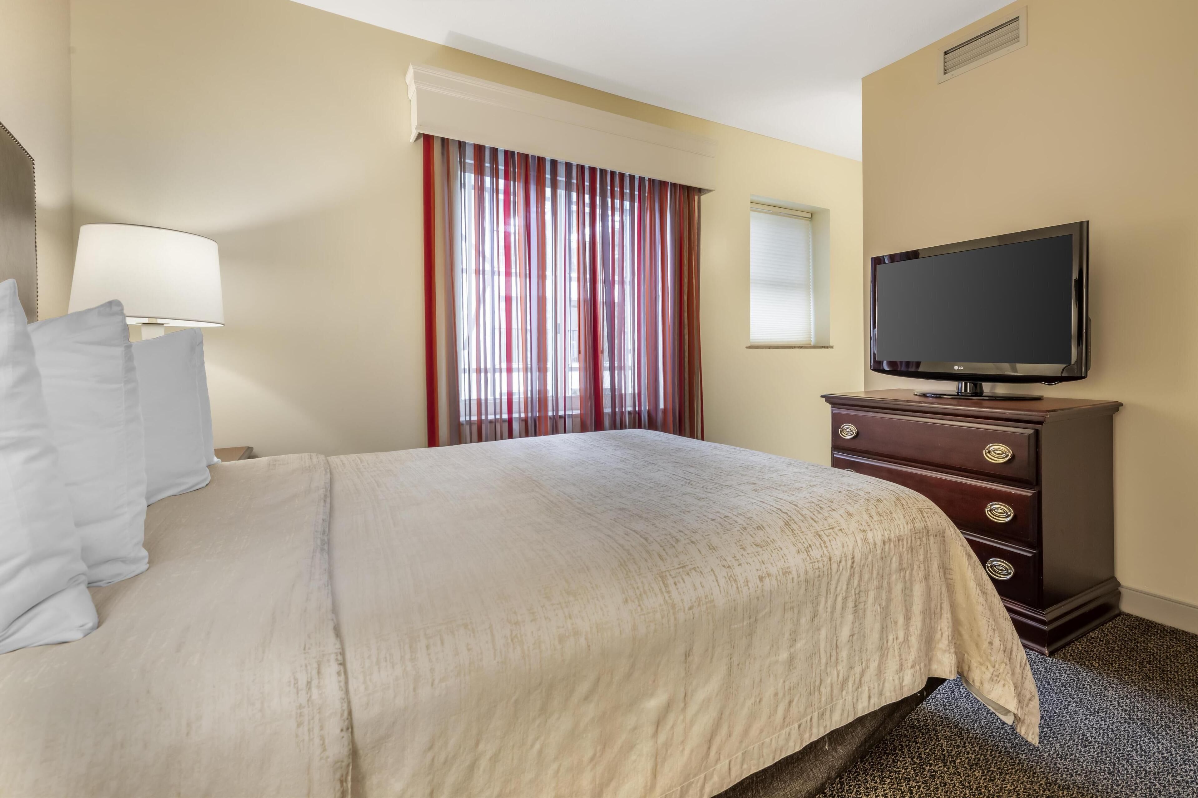 A hotel room with a bed, a TV, a dresser, and a window with curtains.
