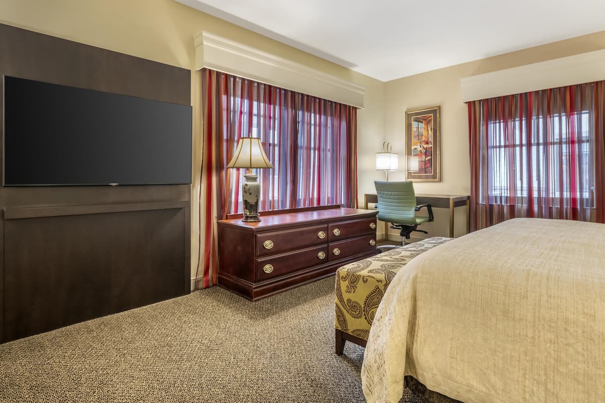 A hotel room with a large bed, a dresser, a desk, a chair, and a television.