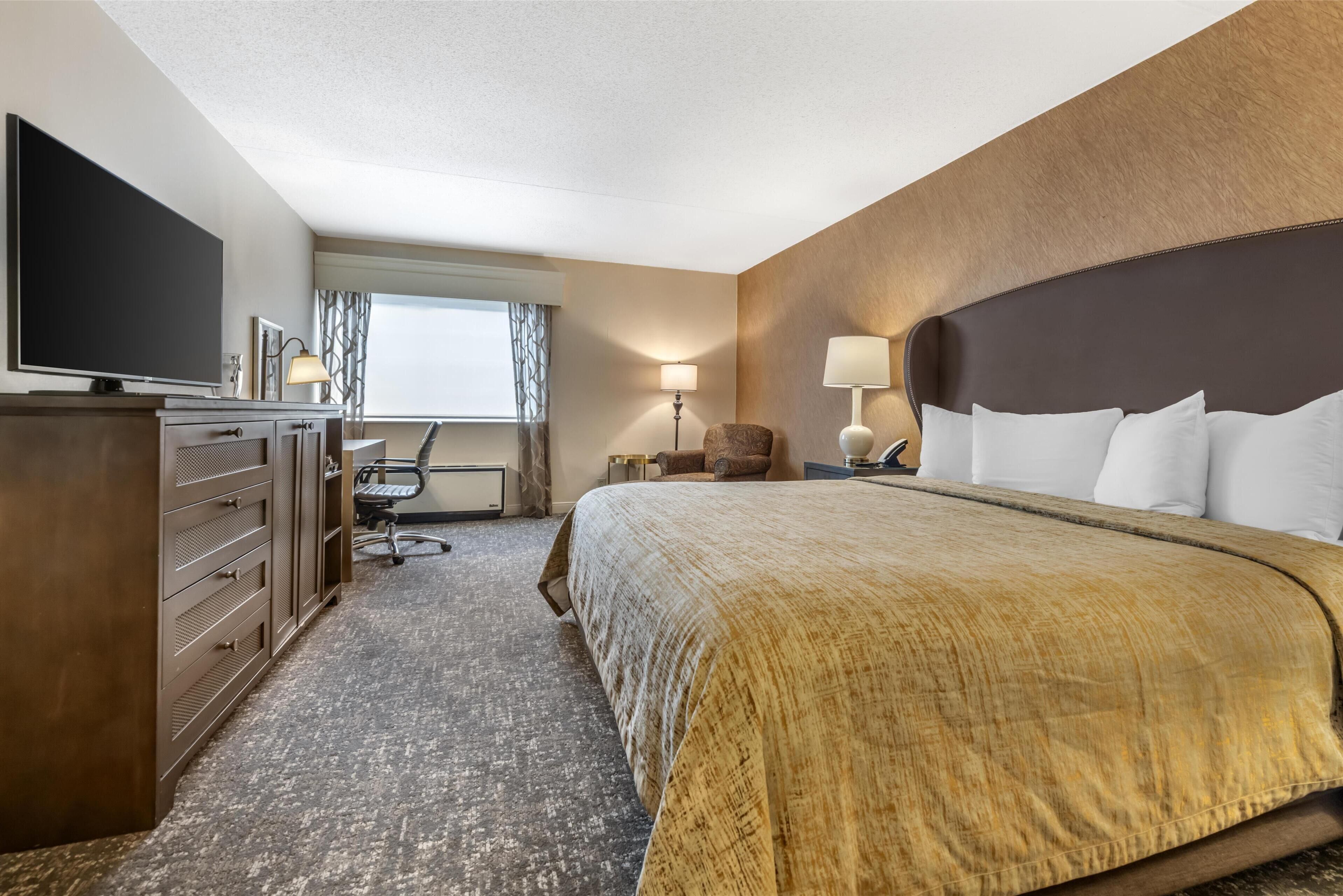 A hotel room with a large bed, a desk, a flat-screen TV, and a window with curtains.