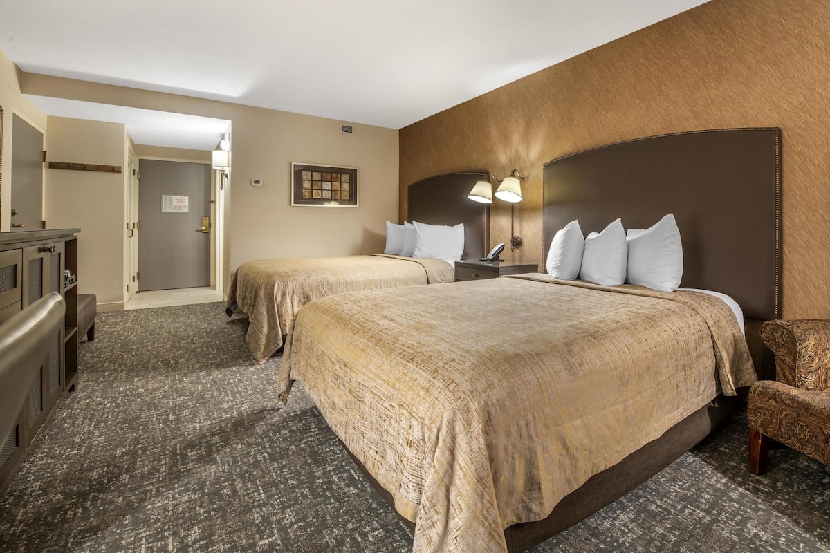 A hotel room with two beds, a desk, a chair, and a bathroom door.