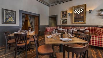 Un restaurant avec des tables et des chaises en bois, un banc à carreaux rouges et blancs, et des œuvres d’art encadrées accrochées aux murs.