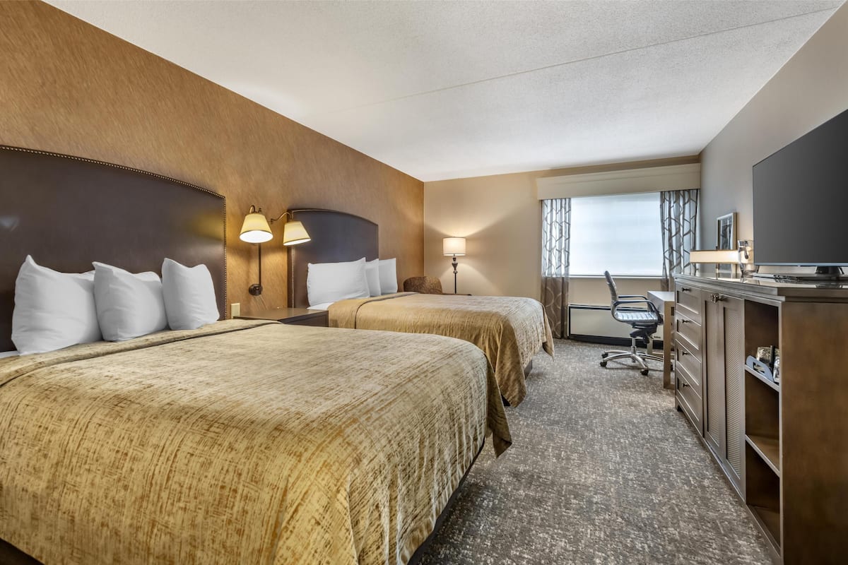 A hotel room with two beds, a desk, a chair, a television, and a window with curtains.