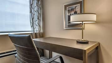 A hotel room with a desk, a chair, a lamp, and a framed picture on the wall.