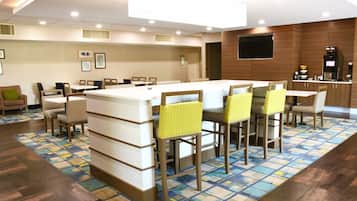 A modern hotel lobby with a central bar area, seating arrangements, and a patterned floor.