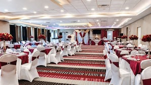 A banquet hall with rows of tables, white chairs, and red drapery.