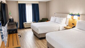 A hotel room with two beds, a desk, a TV, a lamp, and a window with curtains.