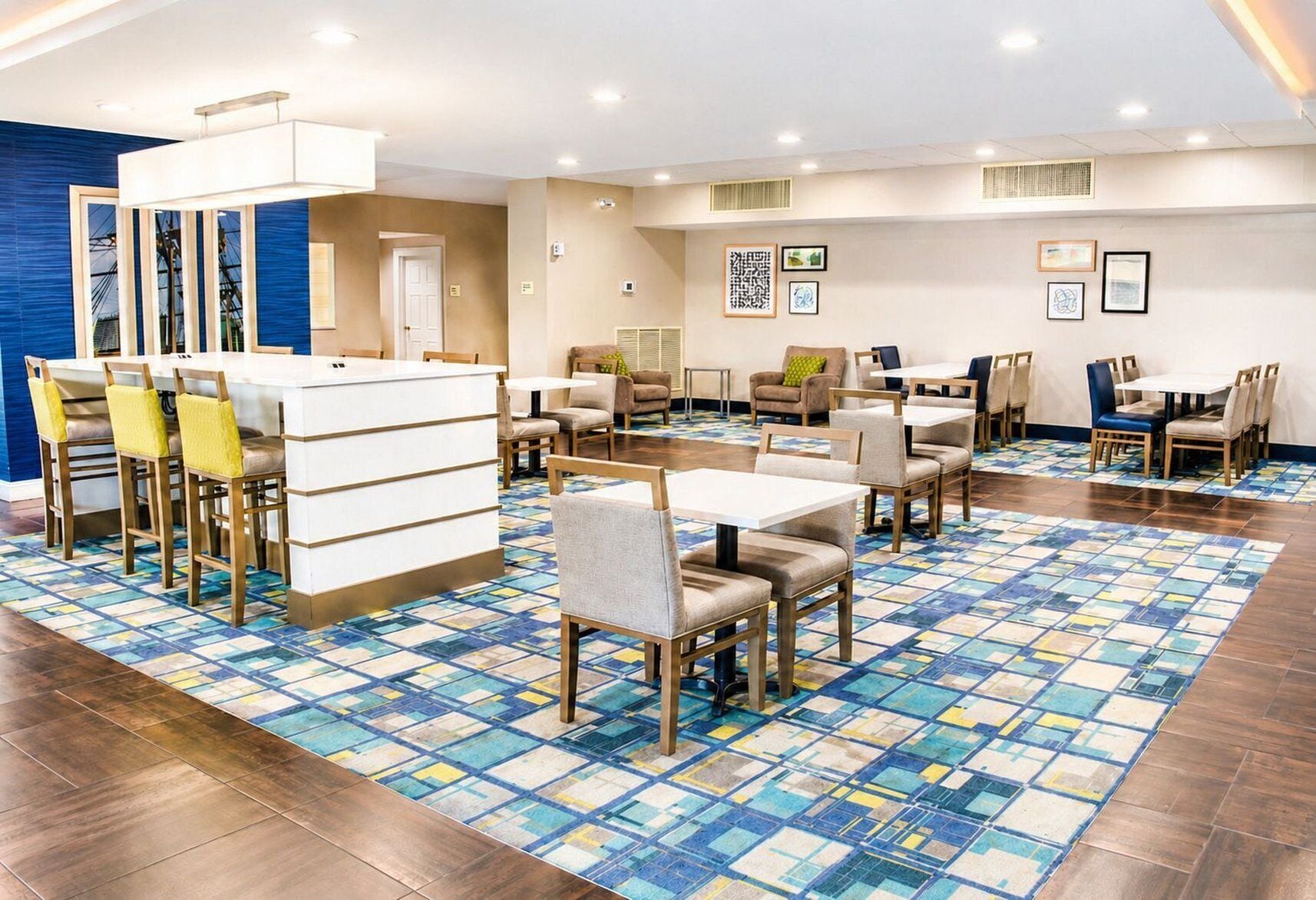 A hotel dining area with multiple tables and chairs, a patterned floor, and artwork on the walls.