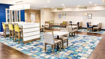 Uma área de refeições de hotel com várias mesas e cadeiras, piso estampado e obras de arte nas paredes.