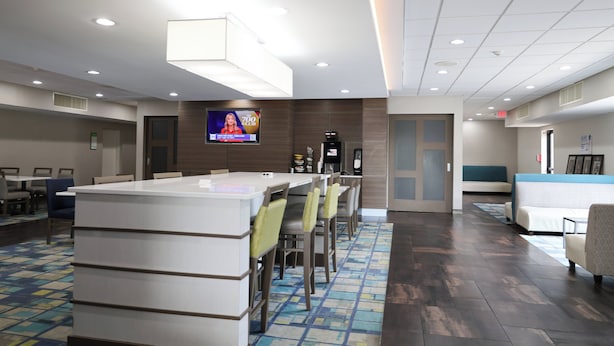 A hotel lobby with a reception desk, seating area, and a television screen displaying an advertisement.
