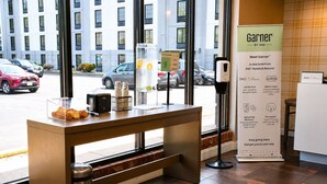 A hotel reception area with a counter displaying a coffee machine, a glass with a beverage, and a signboard advertising hotel amenities.