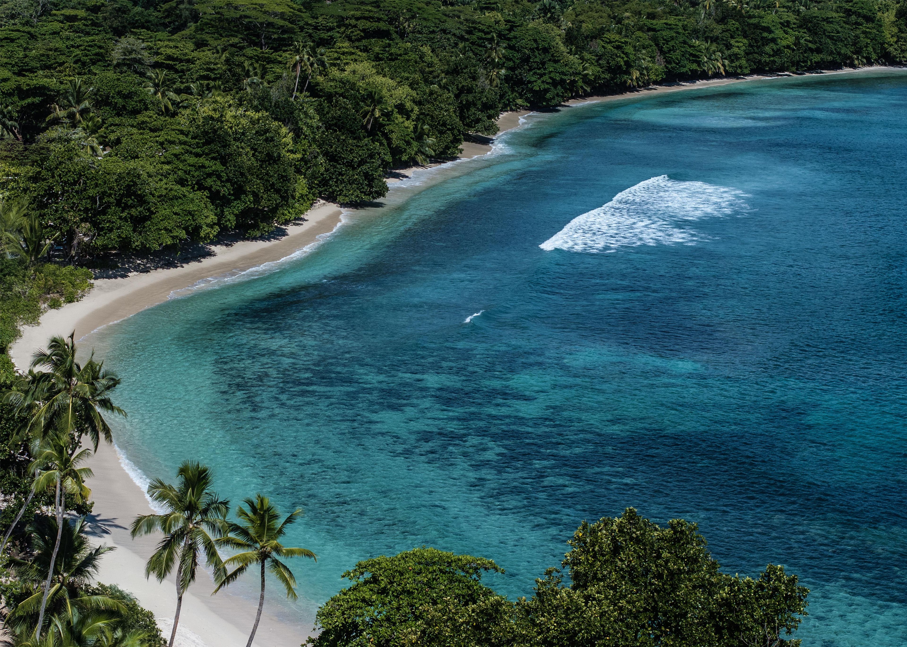 A coastal landscape with a beach, clear turquoise waters, and dense greenery.