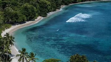A coastal landscape with a beach, clear turquoise waters, and dense greenery.