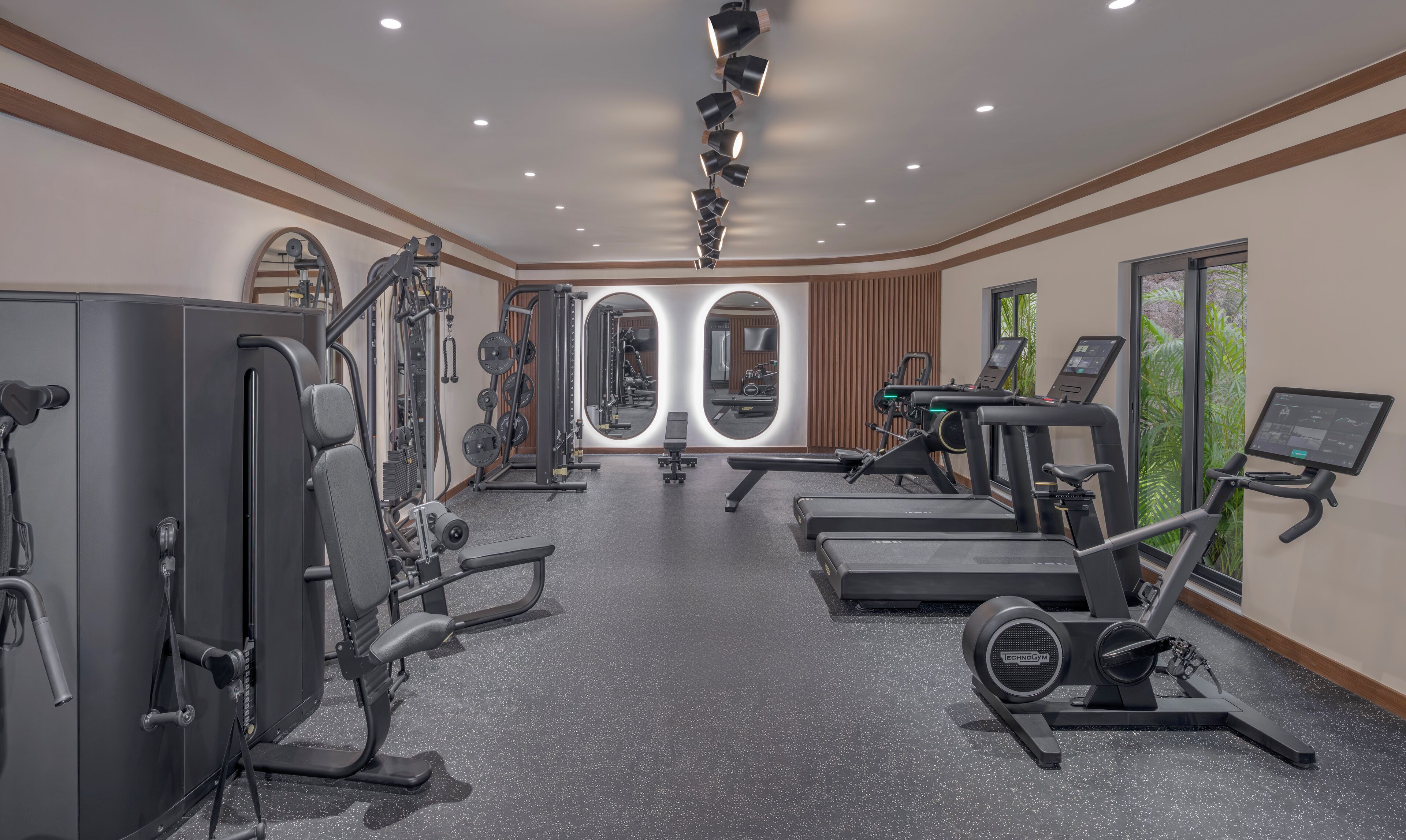 Ett gym med konditionsmaskiner, styrketräningsutrustning och en vägg full med speglar.