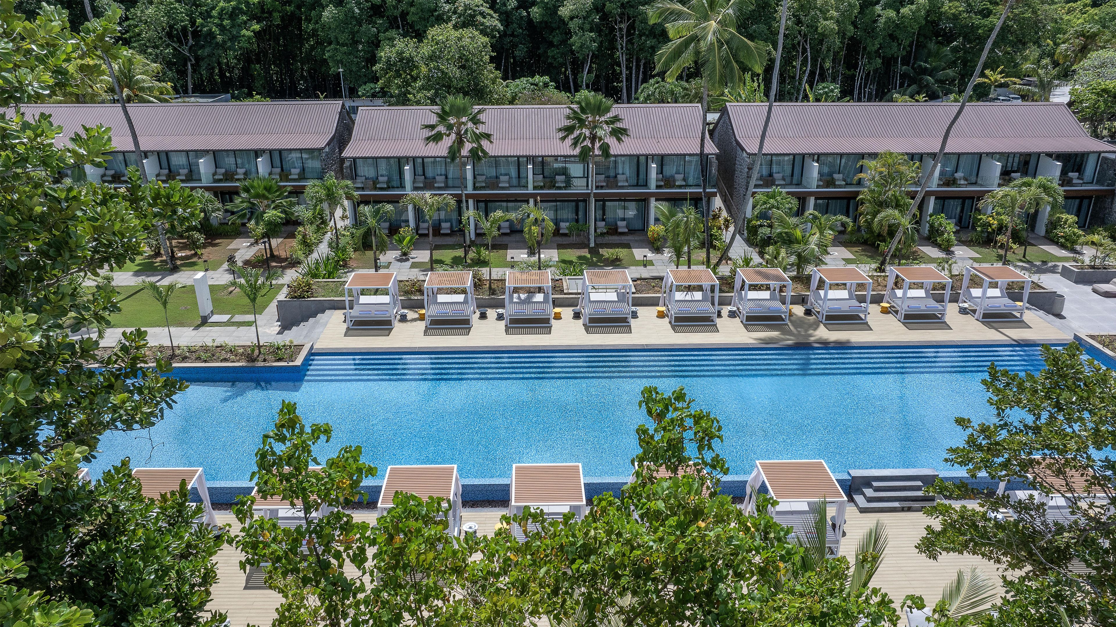 A resort with a swimming pool, lounge chairs, and a building with a tiled roof.