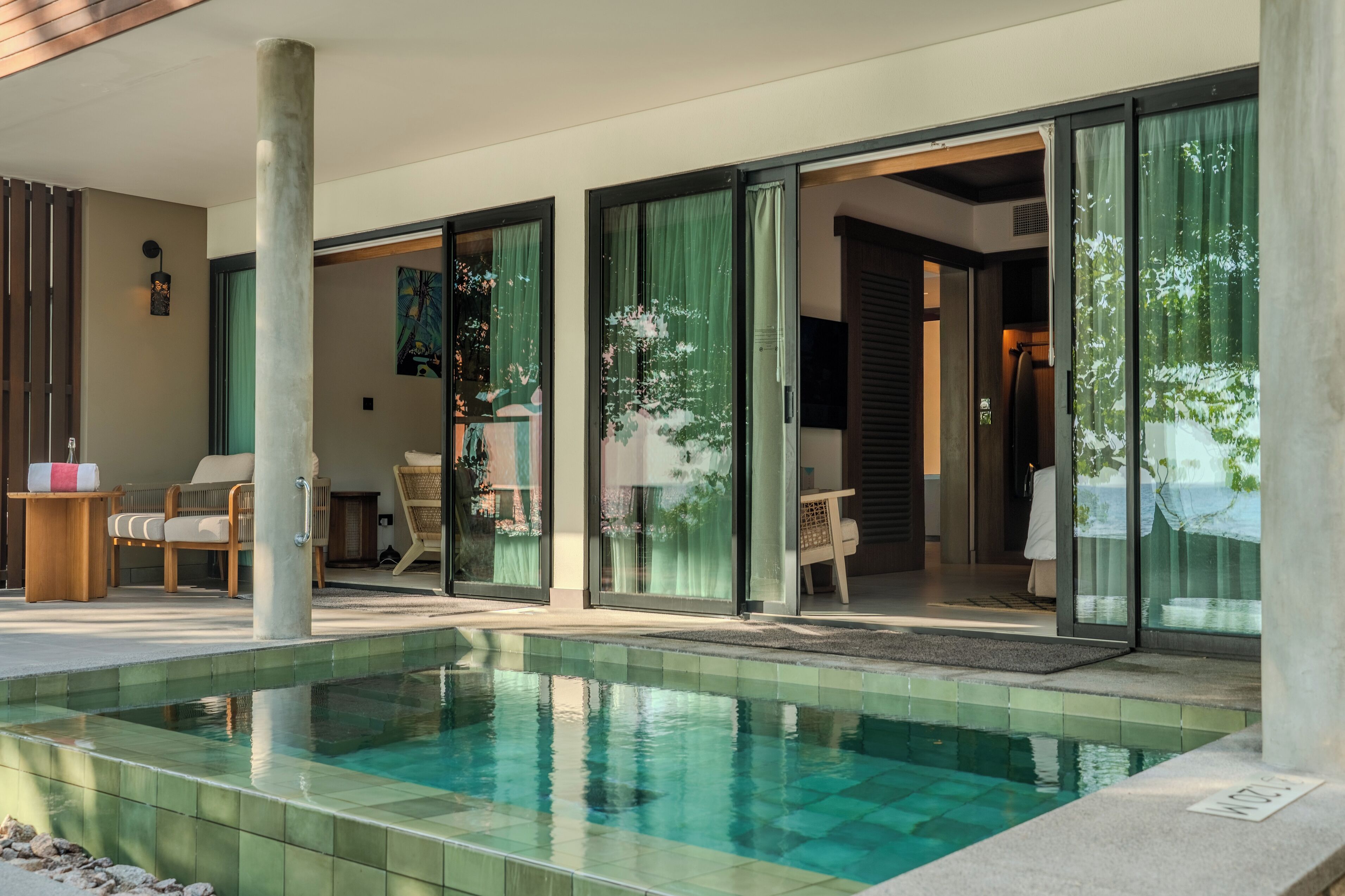 Un espace piscine moderne doté d’une piscine à eau claire, d’une terrasse en bois et d’un coin salon avec des chaises et une table.