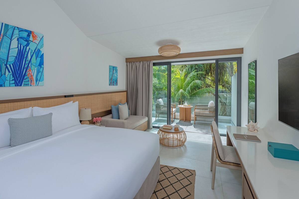 Ein Hotelzimmer mit einem großen Bett, einem Schreibtisch, einem Stuhl, einem Fernseher und Blick auf einen Garten.