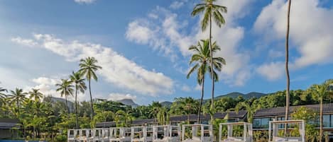 A pool area with lounge chairs and palm trees, surrounded by buildings and a mountainous backdrop.