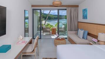 A hotel room with a bed, a desk, a chair, a sofa, a view of the ocean, and a balcony with a table and chairs.