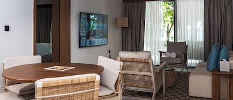A modern living room with a round wooden table, wicker chairs, a sofa, and a television mounted on the wall.