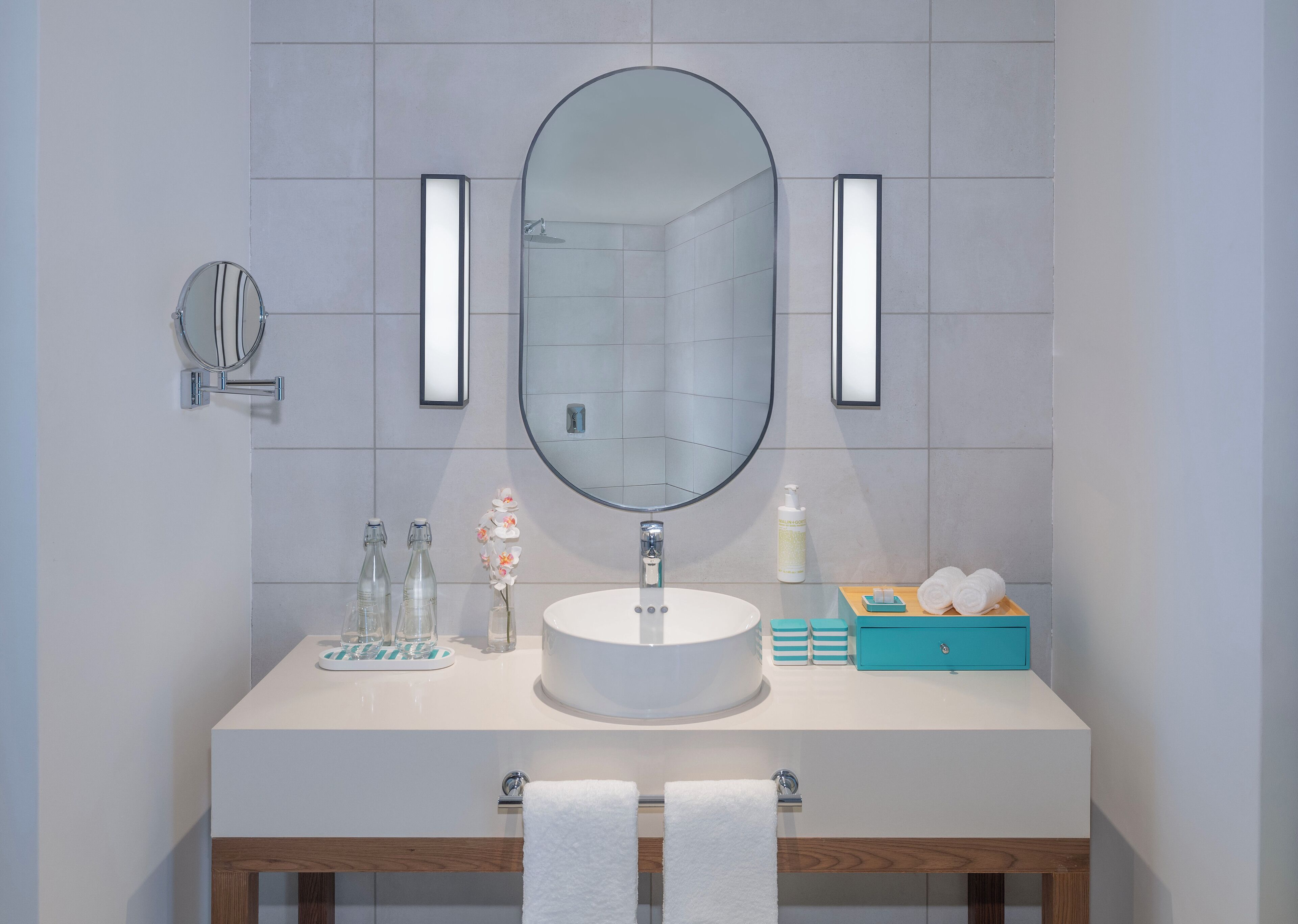 Ein Badezimmer mit rundem Spiegel, zwei Wandleuchten, einem Waschbecken, einem Spiegel, einem Handtuchhalter und einer kleinen Holzeinrichtung.