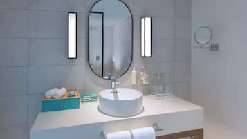 A bathroom with a large oval mirror, a rectangular mirror, and a small round mirror. There is a white sink with a wooden vanity, a towel rack, and a wooden stool.